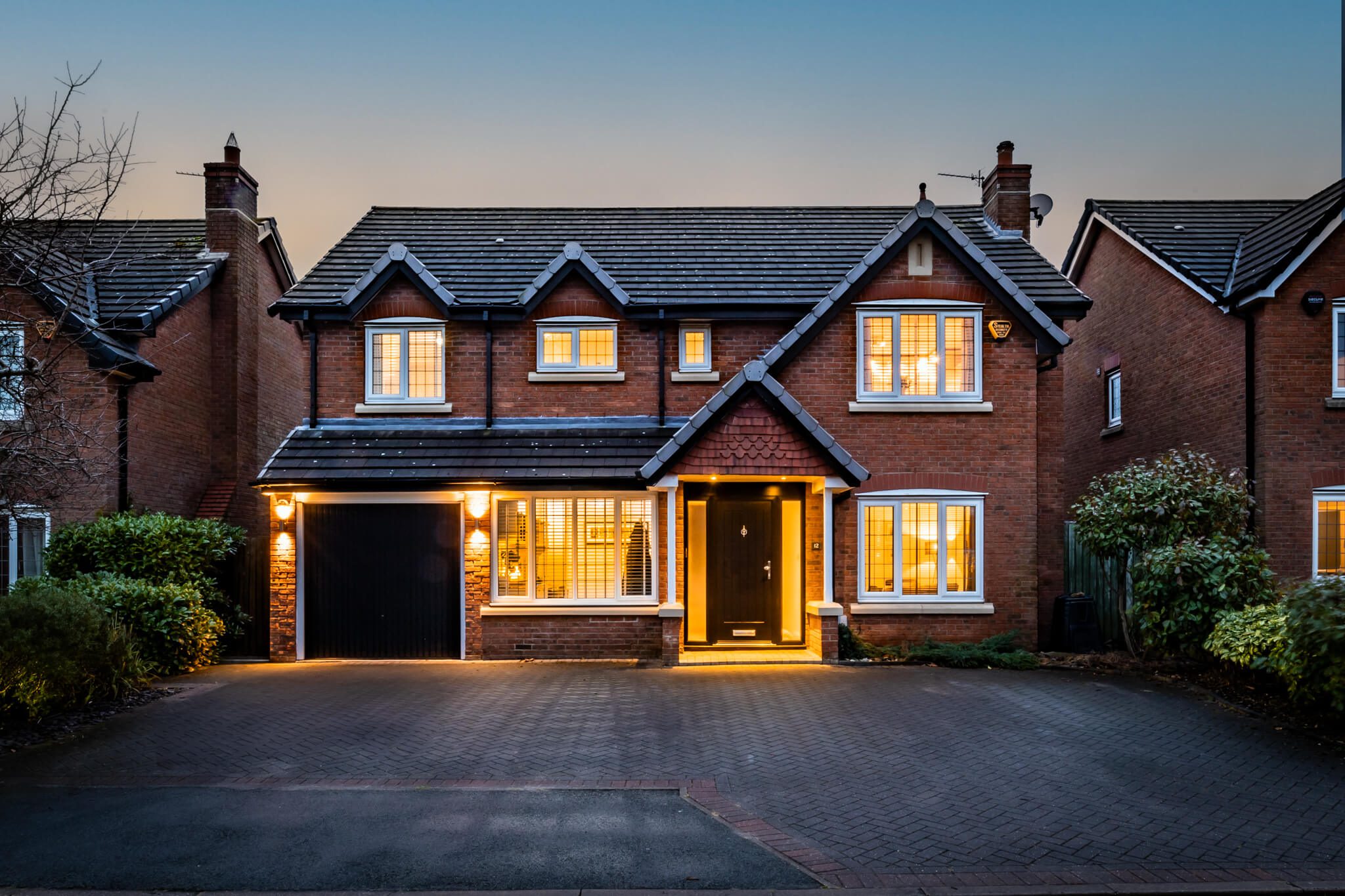 Front twilight view of 12 Houghton Close, Kingsmead, Cheshire with driveway and illuminated windows.