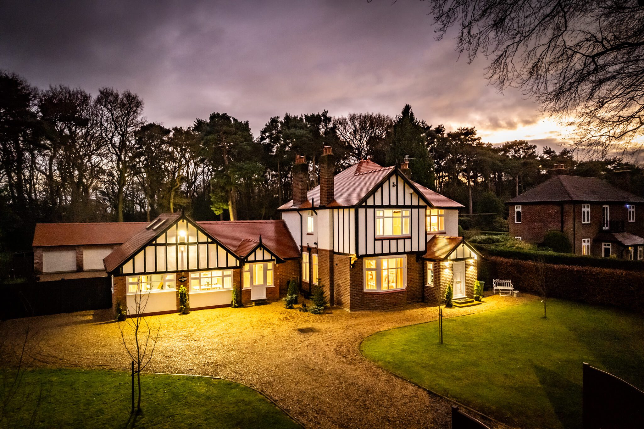 Twilight aerial showing front elevation, driveway and woodland setting at Kennelwood, Sandiway, Cheshire.