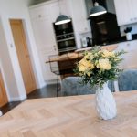 Vase of yellow flowers on dining table in open-plan kitchen of a Kingsmead Cheshire home.