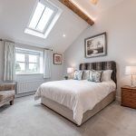 Light-filled double bedroom at Leigh View Barns in Cuddington, Cheshire, featuring a vaulted ceiling with exposed beam and skylight — part of a luxury barn conversion marketed by J Lord & Co.