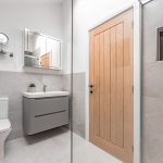 Contemporary shower room with oak door, soft-grey vanity and neutral tiling inside a luxury barn conversion in Cuddington, Cheshire.