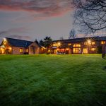 Twilight exterior of Hall Green Barn showing illuminated elevation and landscaped gardens in Acton Bridge