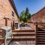 Rear patio entertaining space at The Barns, Bostock Hall Estate, featuring raised terrace, outdoor seating and landscaped garden