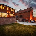 Rear view of Hartford home with garden, patio seating and evening lighting