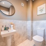 Ground floor WC with neutral tiling, pedestal sink and round mirror