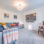 Family lounge at 211 Hartford Road, Davenham, with grey corner sofa, feature chandelier, wall-mounted television and soft neutral décor.