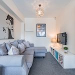 Snug or second sitting room at 1 Castlemead Walk, Kingsmead, with grey corner sofa, wall-mounted television and soft neutral décor.