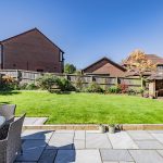 Landscaped rear garden with lawn, patio seating and mature planting at a detached family home in Kingsmead, Northwich.
