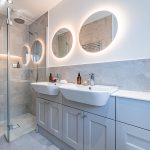 En-suite shower room at 41 Medlock Street, Rudheath, with twin basins, walk-in shower, grey tiling and illuminated round mirrors.