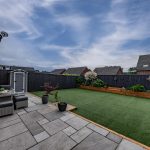 Rear garden seating area at 41 Medlock Street, Rudheath, with paved patio, hanging chair, outdoor sofa and raised planted borders.