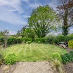 Formal rear garden at Brooklyn Cottage with mature planting, shaped lawns and a private countryside backdrop.