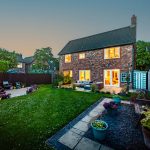 Twilight rear elevation with illuminated interior and landscaped garden.