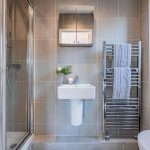 Contemporary en suite shower room with glazed enclosure, grey wall tiles, pedestal basin and chrome towel radiator.