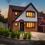 Detached brick home with illuminated leaded windows, landscaped frontage and feature planting at twilight.