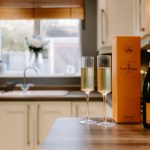 Kitchen lifestyle detail with champagne and two glasses arranged on the breakfast bar against a softly focused interior.
