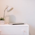 Bedroom detail featuring a white chest of drawers, desk lamp, small plant and closed laptop.