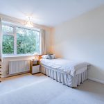 Bedroom with single bed, wooden chest of drawers and wide window overlooking mature trees and greenery.